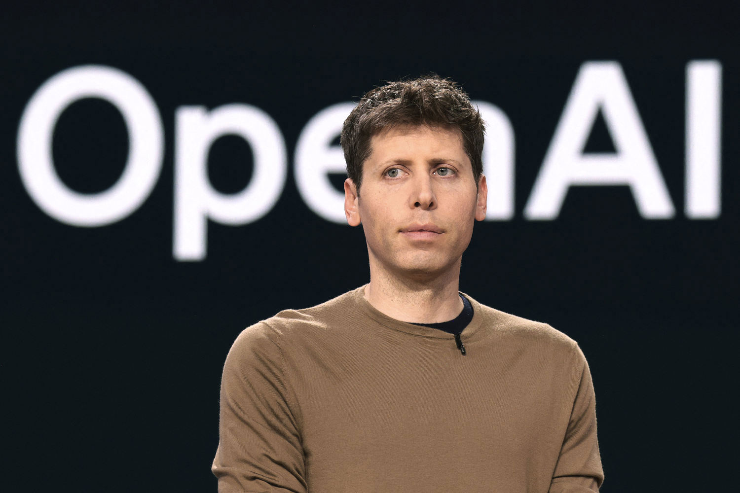 Sam Altman ยืนหน้าโลโก้ OpenAI