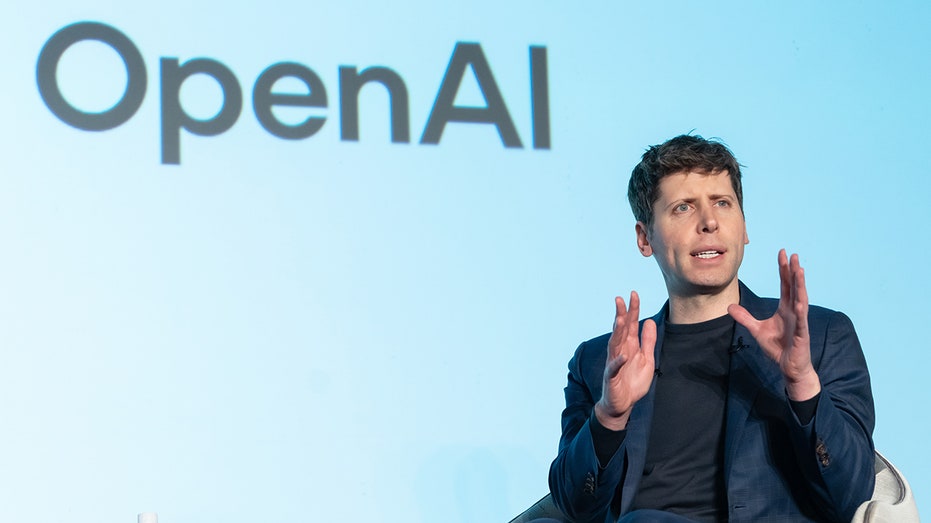 Sam Altman ขึ้นพูดบนเวทีต่อหน้าโลโก้ OpenAI