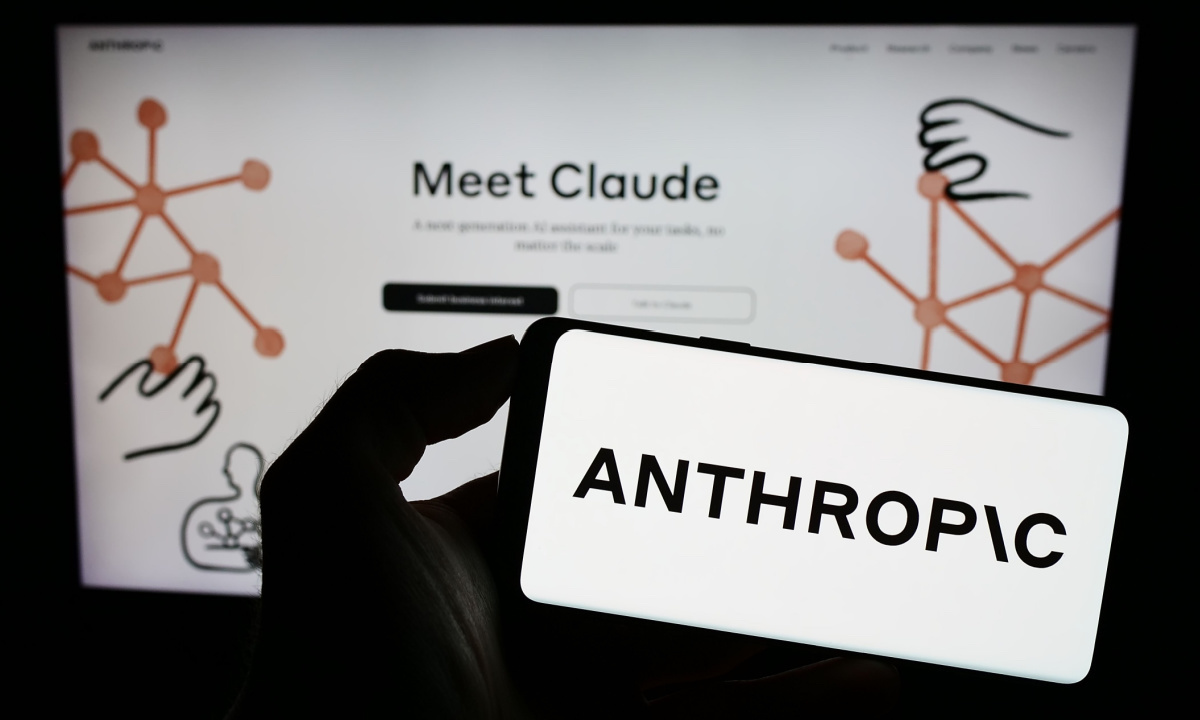 คนถือโทรศัพท์ที่มีโลโก้ Anthropic อยู่หน้าจอเว็บไซต์ Claude