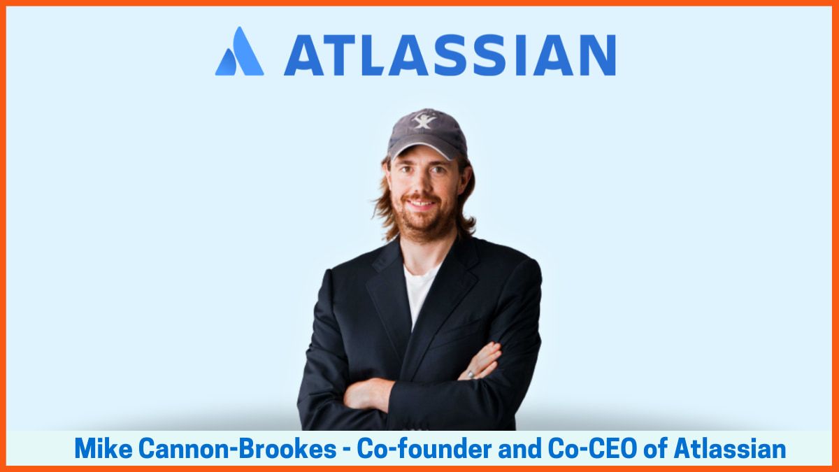 Mike Cannon-Brookes ยืนกอดอกหน้าโลโก้ Atlassian